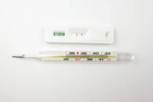 Ein Quecksilberthermometer und eine negative COVID-19-Testkassette auf weißem Hintergrund.